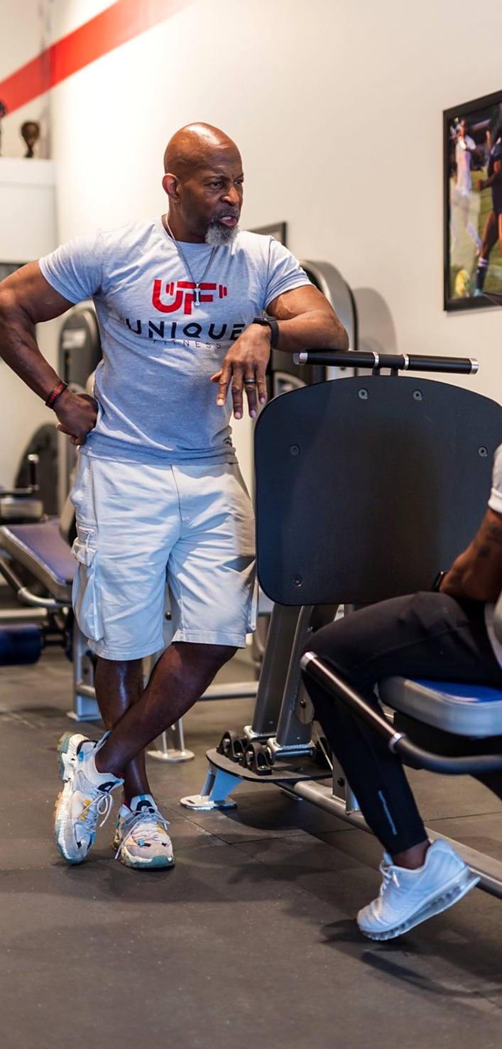 Ron beside a participant using the leg press in the Unique Fitness studio